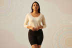 "Confident Indian woman wearing only sleek black waist shapewear fro botto to up, standing tall with poise, soft golden light, modern yet cultural vibe, showcasing smooth curves and strength, empowering, minimalistic elegance, rich warm tones." get  bg wit ligt colours and cover te upper bra wit a top wic just dont cover te sapewear